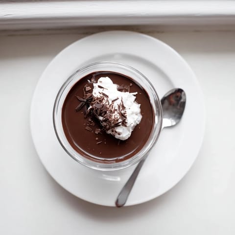 Creamy chocolate pudding layered in a small glass with fresh raspberries and a mint garnish