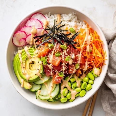 A colorful Poke Bowl topped with creamy avocado slices, crisp cucumber, julienned carrots, and edamame on a bed of fluffy rice.