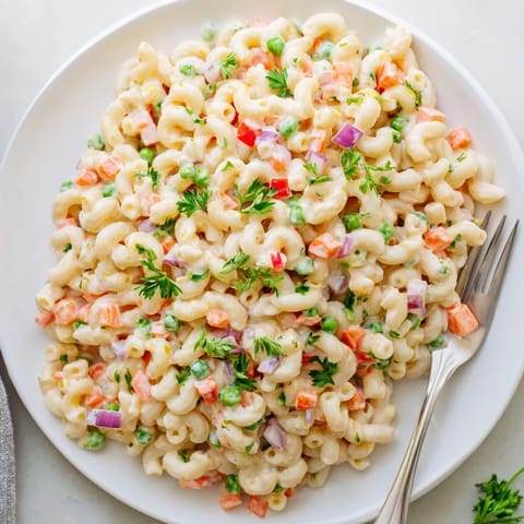 Colorful macaroni salad featuring elbow pasta, bell peppers, and peas, served in a clear glass dish.