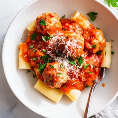 Baked turkey meatballs on a white plate next to a bowl of marinara, fresh parsley garnish, and a fork for serving.