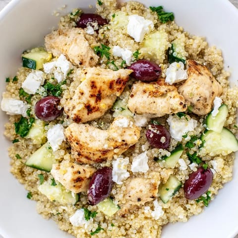 Serving suggestion for Mediterranean Chicken Bowl: a forkful of seasoned chicken, olives, and crisp cucumbers over quinoa.  