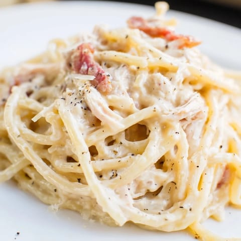 A warm skillet of chicken carbonara topped with grated Parmesan and fresh parsley, steam rising from the pasta.