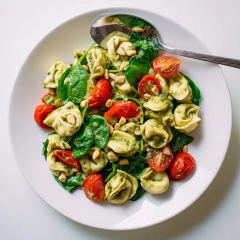 Perfectly cooked Pesto Tortellini Salad served on a white platter, garnished with toasted pine nuts and grated Parmesan for a summer picnic.  