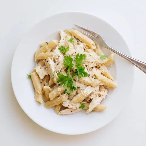 A close-up view of Roasted Garlic Chicken Penne in a white bowl, showcasing the silky sauce clinging to each pasta piece.