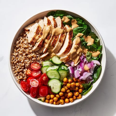 A vibrant Lemon Tahini Chicken Power Bowl with roasted chicken, farro, chickpeas, and fresh vegetables, drizzled with creamy sauce.