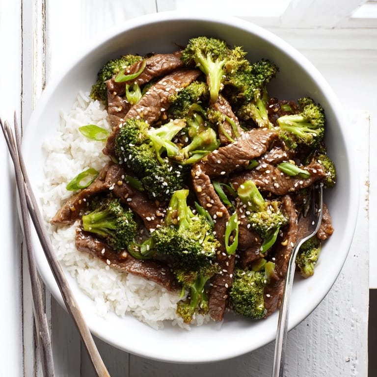 Tender beef and crisp broccoli sizzling in a savory soy-garlic sauce, prepared in a stainless steel skillet for a quick dinner.