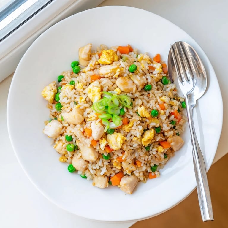 A close-up of golden-brown Chicken Fried Rice, garnished with extra spring onions, served next to a small bowl of chili sauce.