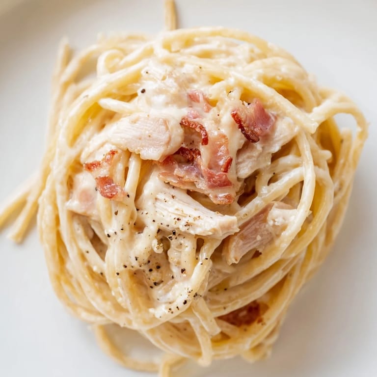 Close-up of chicken carbonara in a shallow bowl, featuring tender shredded chicken, spaghetti, and a velvety black pepper sauce.