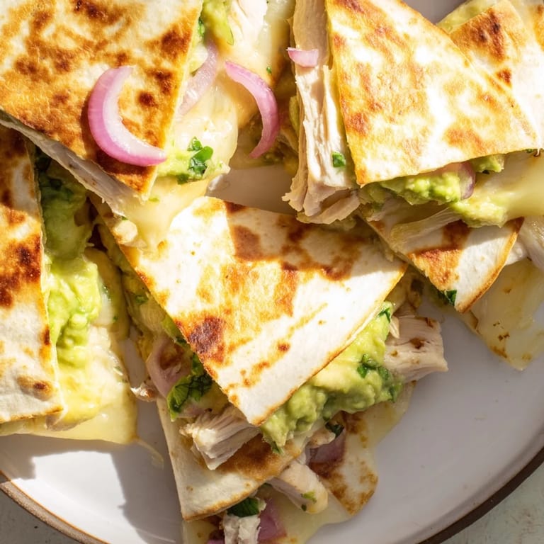 A close-up view of a warm Chicken Avocado Quesadilla revealing melted cheese, grilled chicken, and creamy avocado filling.  