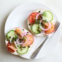 Golden toasted bagel halves generously spread with creamy white cream cheese, topped with fresh dill and sliced red onion for a savory bite.