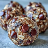 Close-up of homemade Banana Chocolate Chip Energy Balls on a rustic wooden board, showing their chewy texture and glistening chocolate chips for a healthy snack.